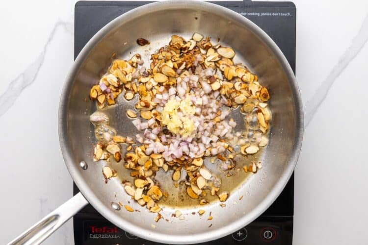 minced shallot and garlic added to toasted sliced almonds in a skillet.