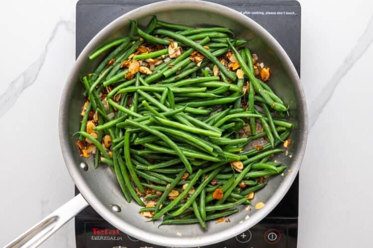 blanched green beans added to a skillet of toasted almonds.