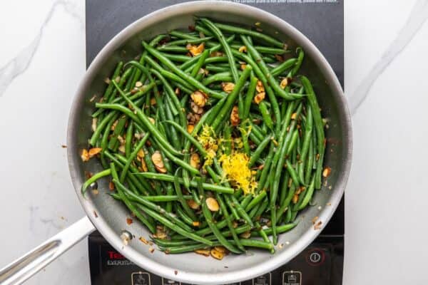 lemon zest added to green bean almondine in a skillet.