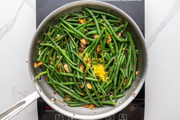 lemon zest added to green bean almondine in a skillet.