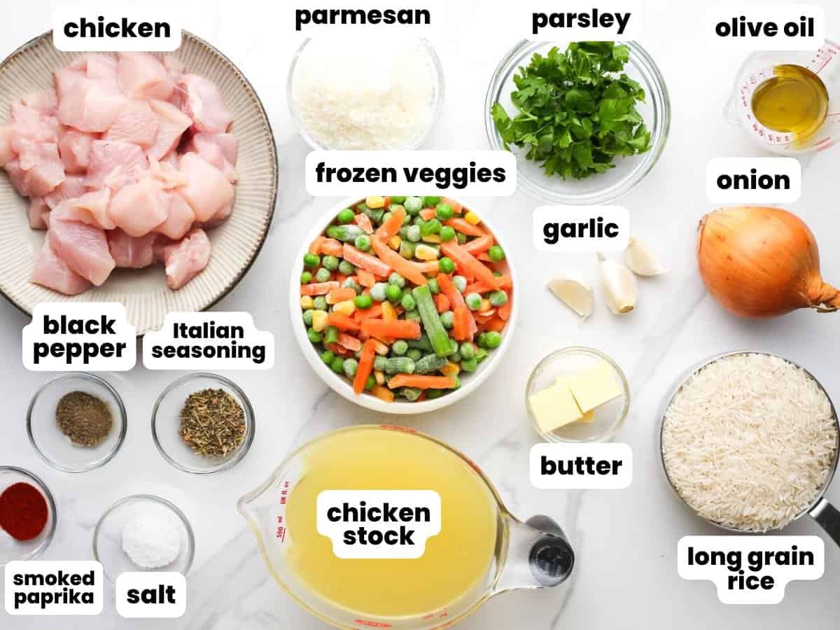 Ingredients for an easy one pot chicken and rice recipe, including rice, chicken, broth, frozen veggies, and seasoning. All of the ingredients are measured and set up in small glass bowls on a marble counter.