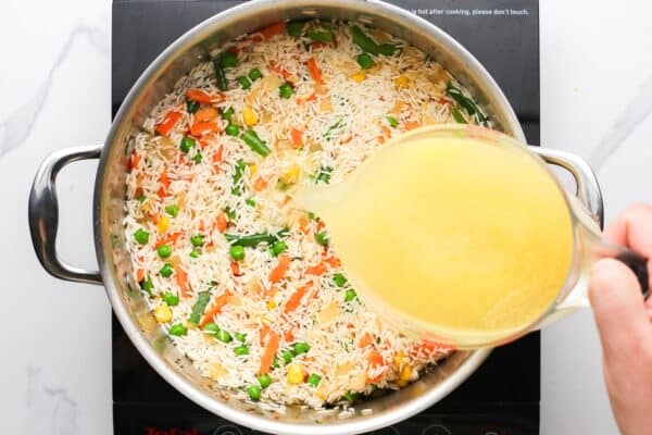 chicken stock poured into a large pot with rice and veggies.