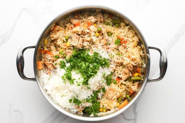 fluffy rice with chicken and mixed vegetables in a pot. chopped herbs and shredded parmesan are added.