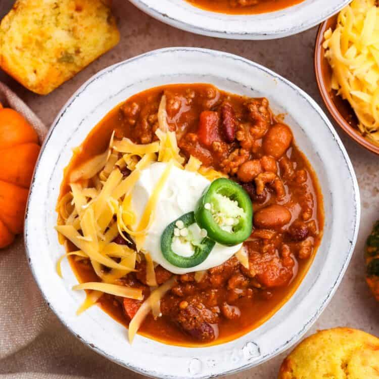 over head view of white ceramic bowls of pumpkin chili topped with sour cream, sliced jalapeno, and shredded cheese.
