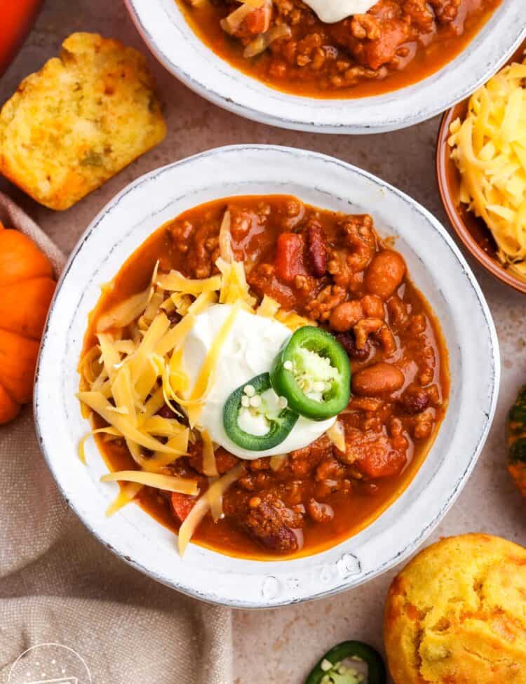 over head view of white ceramic bowls of pumpkin chili topped with sour cream, sliced jalapeno, and shredded cheese.
