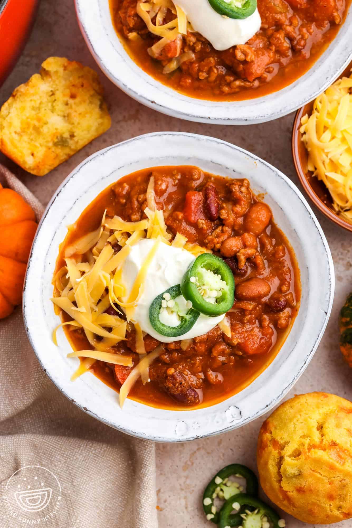over head view of white ceramic bowls of pumpkin chili topped with sour cream, sliced jalapeno, and shredded cheese.
