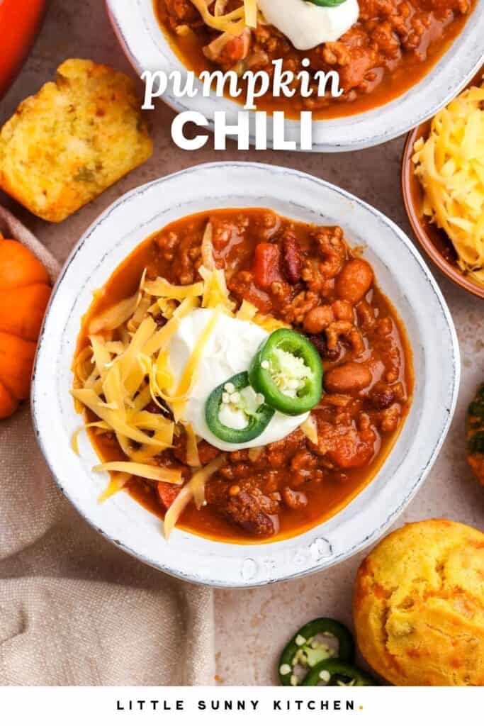 bowls of chili made with pumpkin, topped with sour cream, cheese, and jalapeno. Text overlay says "pumpkin chili"