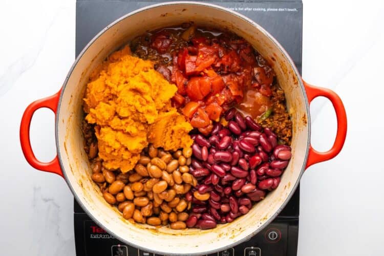 pumpkin puree, two types of beans, and diced tomatoes added to a pot of chili.