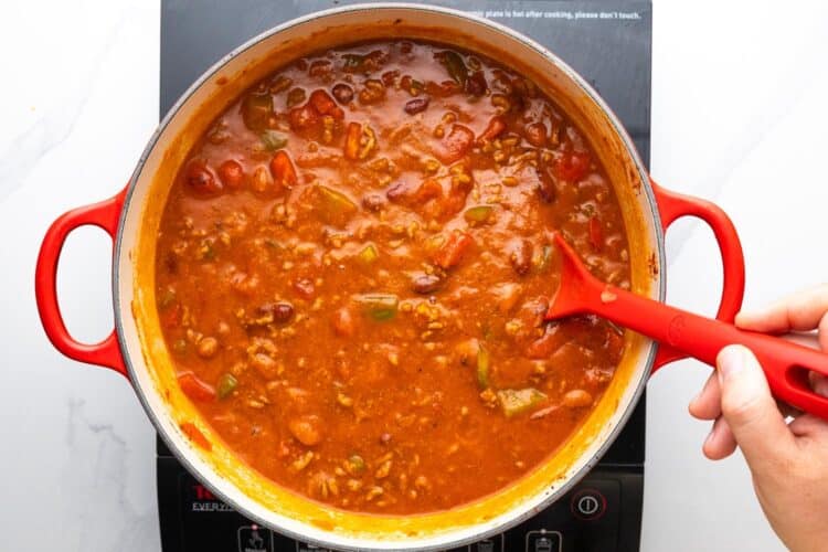 beef chili in a thick pumpkin sauce, cooking over a burner, stirred with a red spoon.
