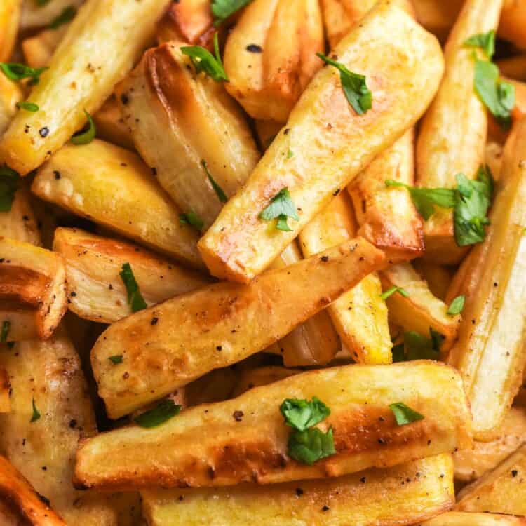 Close-up of roasted parsnips with crispy edges and chopped parsley in a white serving bowl.