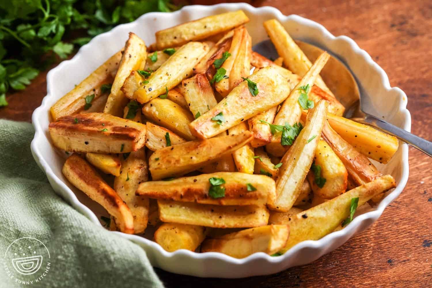 Bowl of golden honey roasted parsnips garnished with fresh parsley, served on a wooden table.