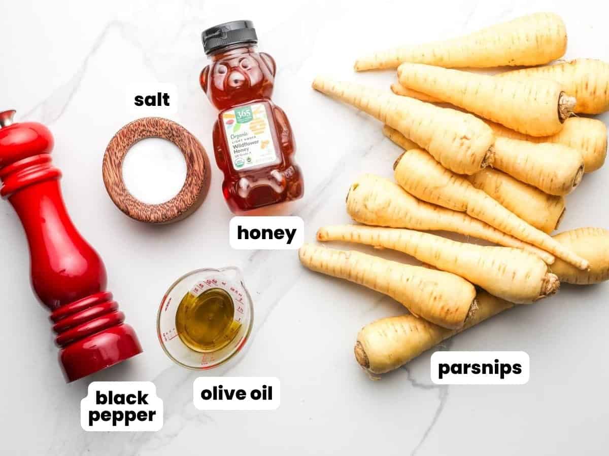 Ingredients for honey roasted parsnips including parsnips, honey, olive oil, salt, and black pepper arranged on a marble surface.