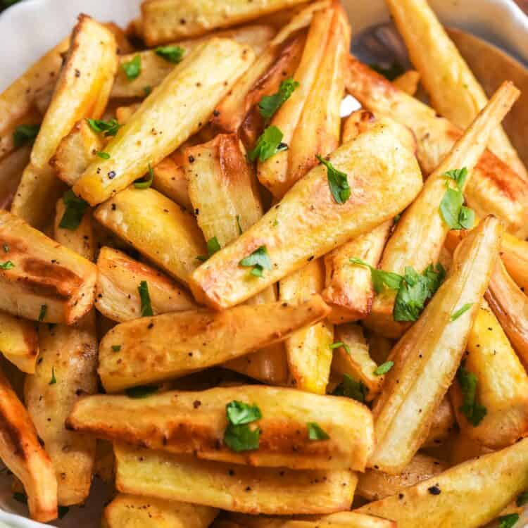 Bowl of golden honey roasted parsnips garnished with fresh parsley, served on a wooden table.