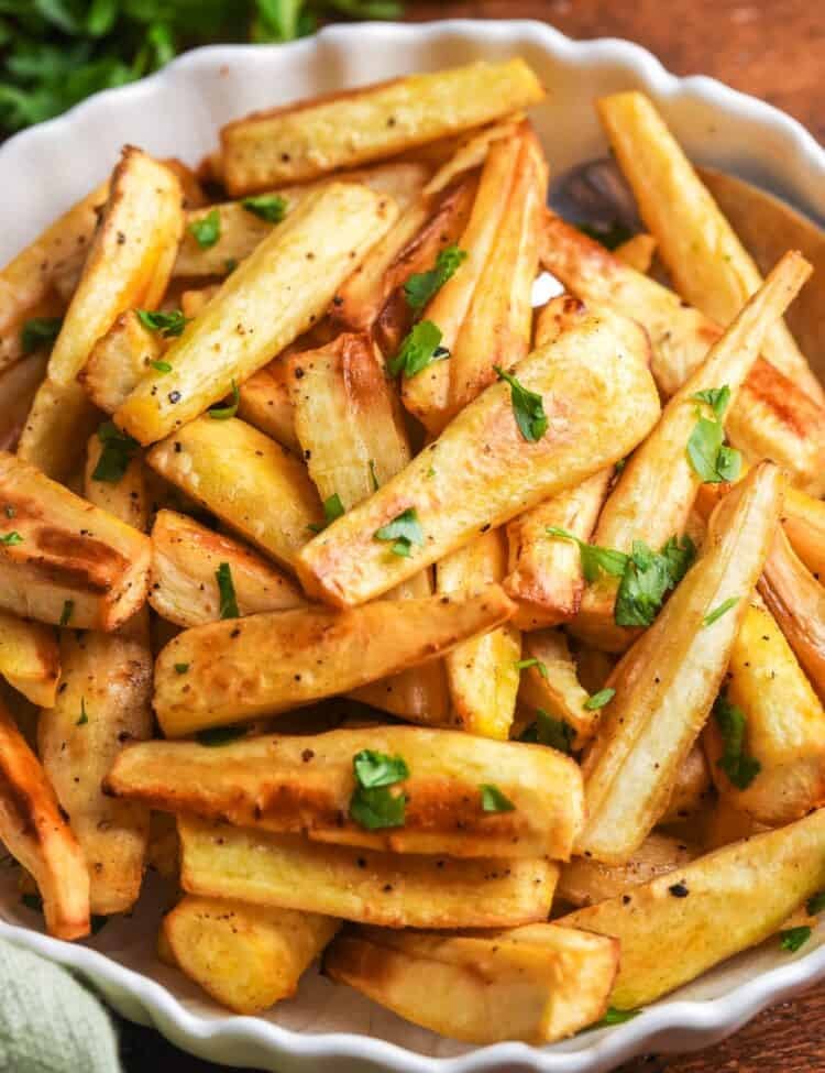 Bowl of golden honey roasted parsnips garnished with fresh parsley, served on a wooden table.