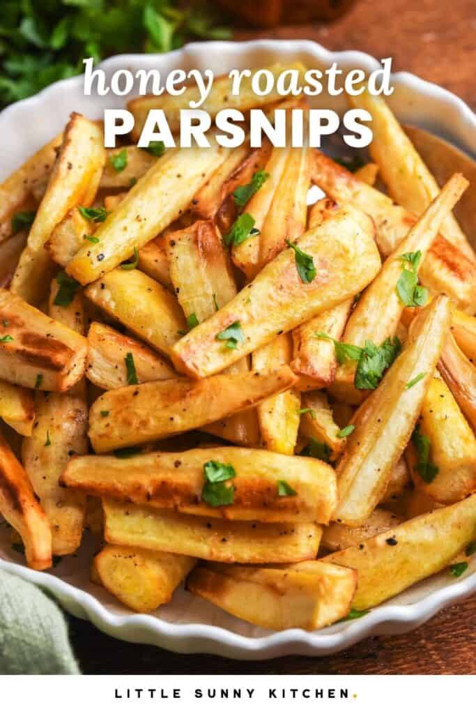 Bowl of golden honey roasted parsnips garnished with fresh parsley, served on a wooden table. And overlay text that reads "honey roasted parsnips"
