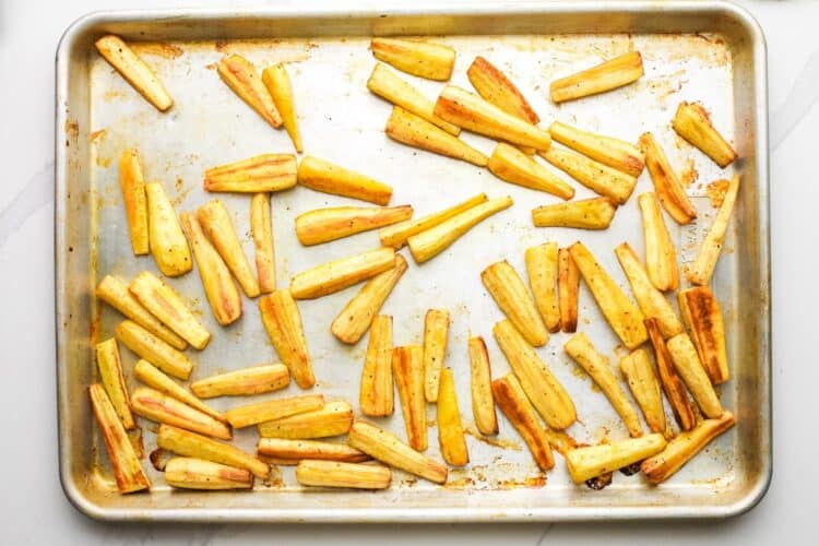 Roasted parsnips on a baking sheet with golden caramelized edges after baking.