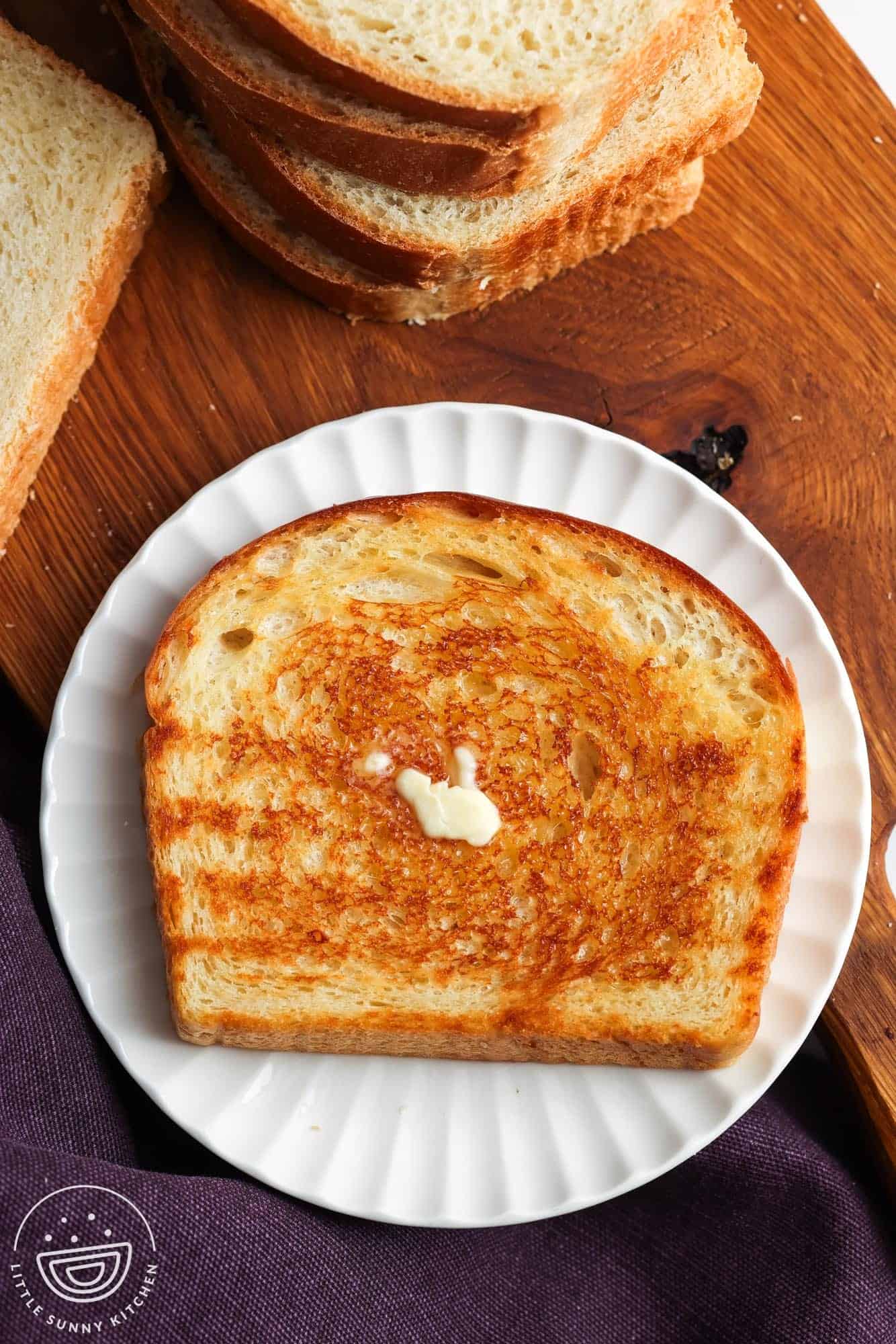 A slice of golden toast with melted butter placed on a white small plate