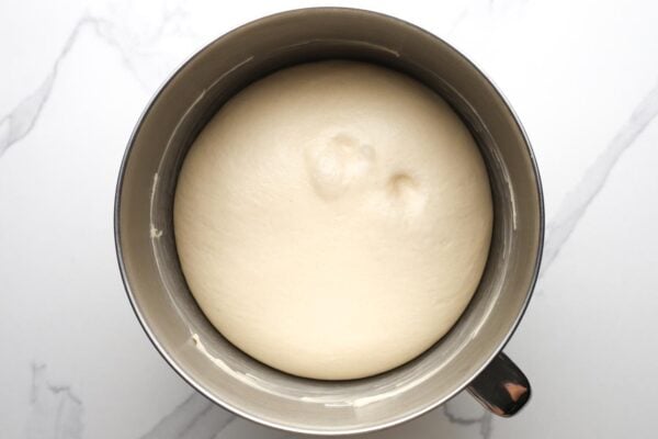 bread dough risen in a metal mixing bowl that is coated with butter.
