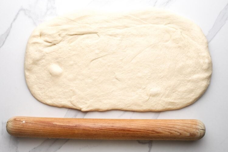 white bread dough rolled out on a marble surface into a rough rectangle.