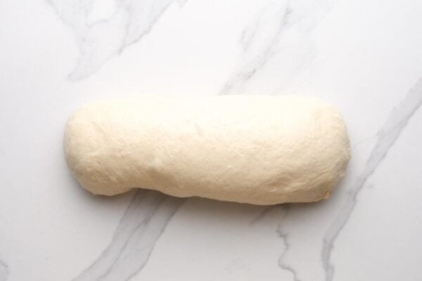 Bread dough rolled up and shaped into a loaf on a marble surface