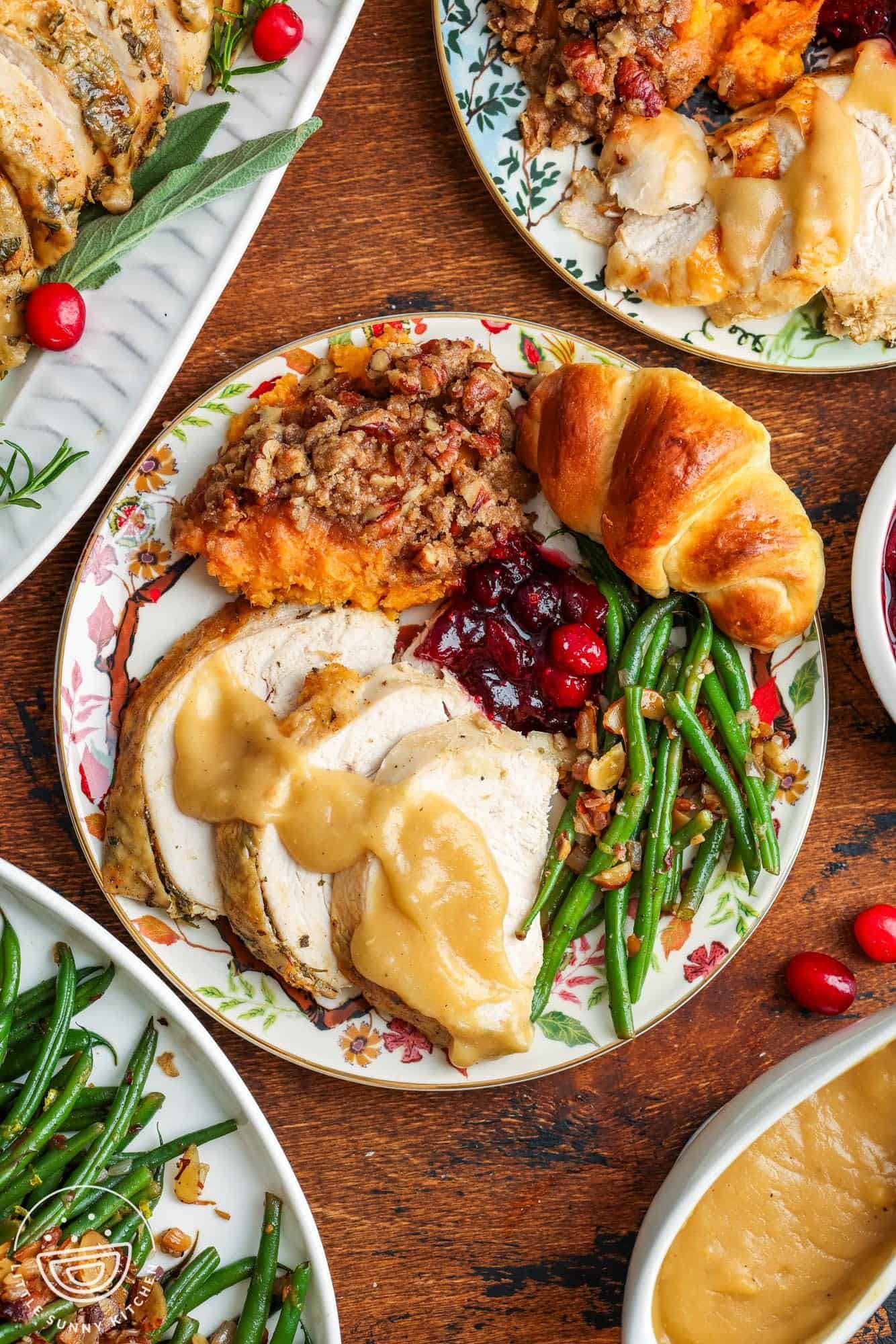 a thanksgiving dinner plate of sliced turkey breast with gravy, green beans almondine, cranberry sauce, sweet potato casserole, and a crescent roll.