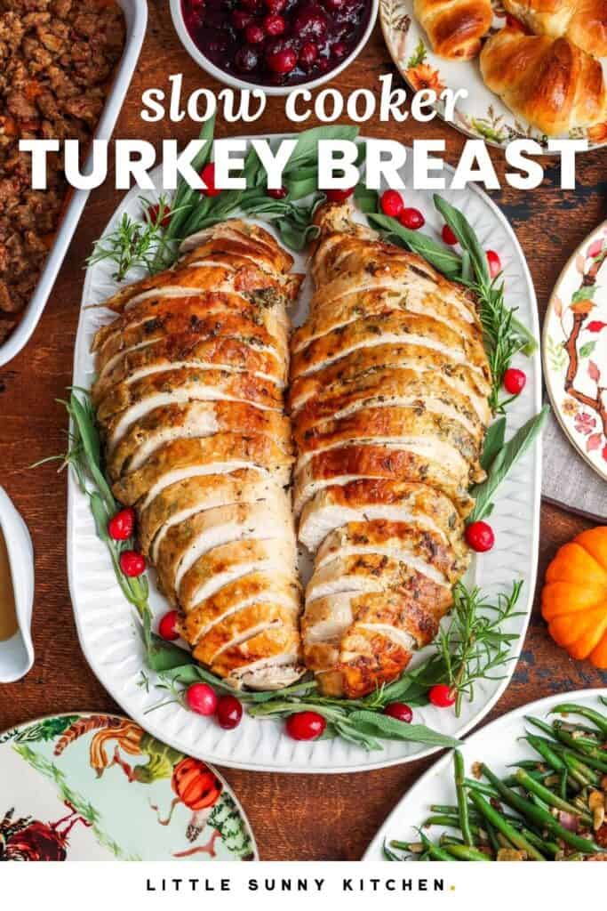 sliced turkey breast on a platter garnished with fresh herbs and cranberries. The turkey platter is in the middle with other side dishes around it, including cranberries, stuffing, green beans, and crescent rolls. Text overlay says "slow cooker turkey breast"