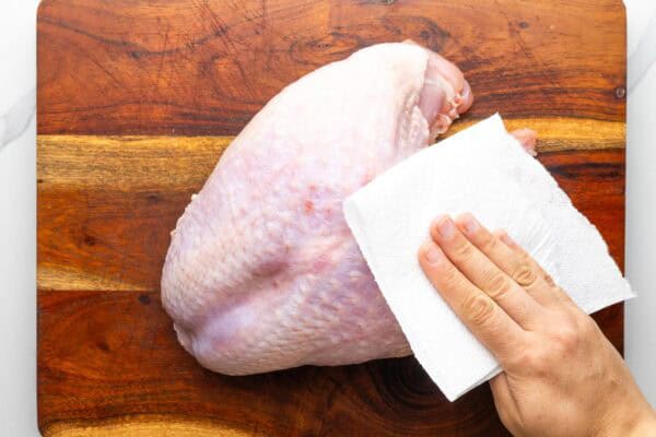 a hand using a paper towel to dry a raw turkey breast.
