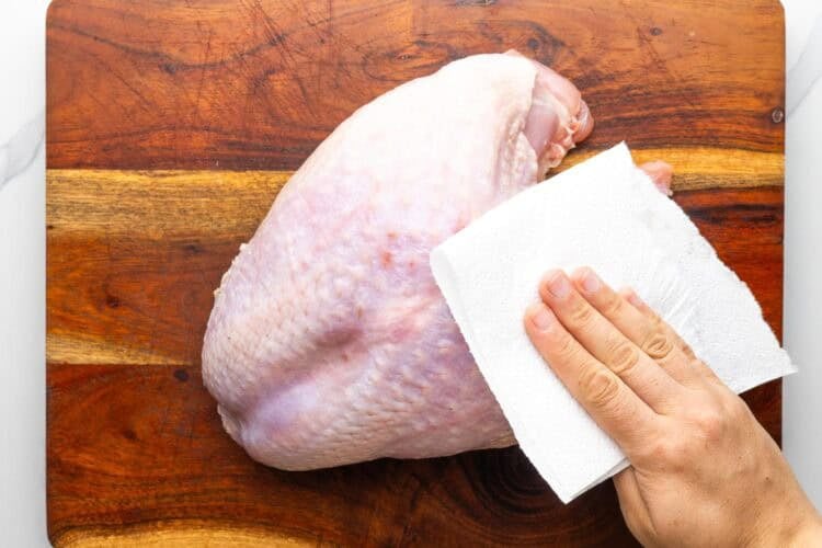 a hand using a paper towel to dry a raw turkey breast.