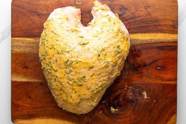 raw turkey breast on a cutting board, coated with seasoned herb butter.