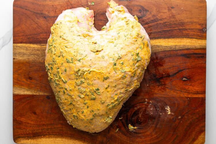 raw turkey breast on a cutting board, coated with seasoned herb butter.