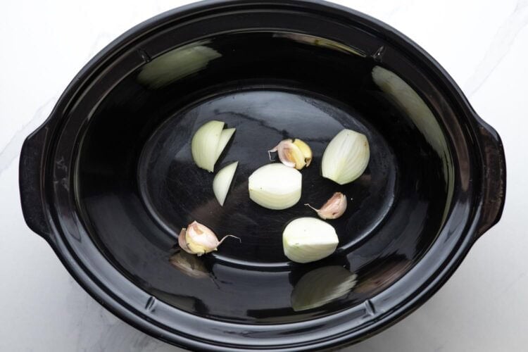 garlic and quartered onion in the bottom of a slow cooker.