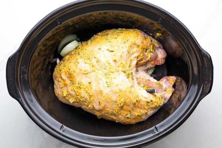 seasoned turkey breast added to a black oval slow cooker insert.