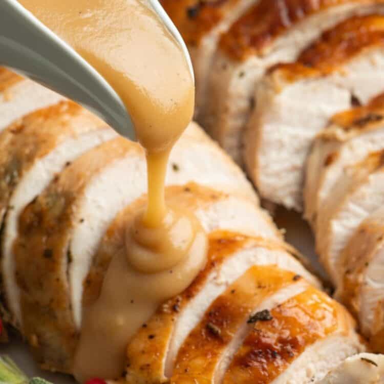 a gravy boat pouring turkey gravy over sliced roasted turkey breast.
