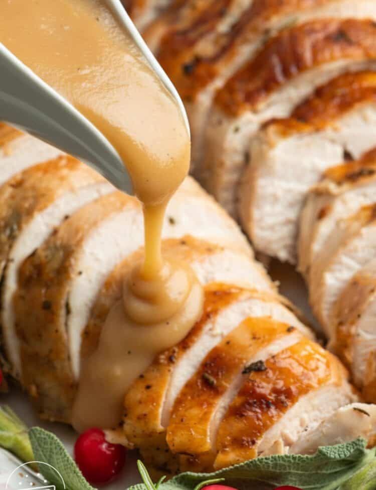 a gravy boat pouring turkey gravy over sliced roasted turkey breast.