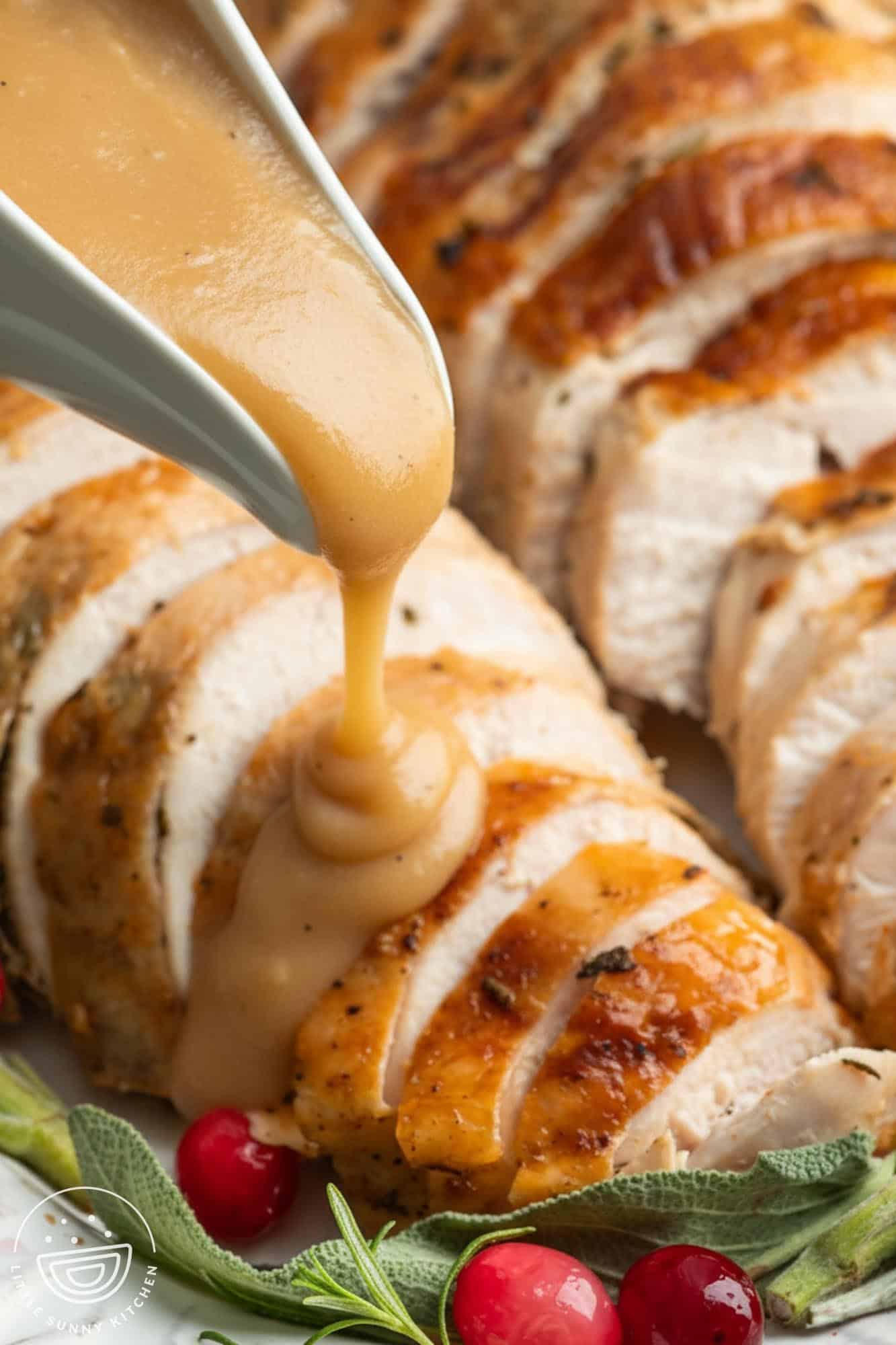 a gravy boat pouring turkey gravy over sliced roasted turkey breast.