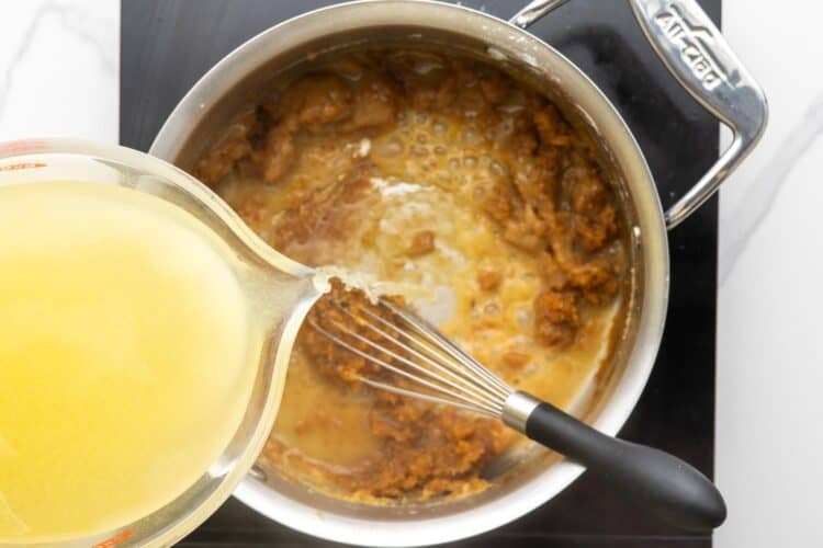 additional chicken stock added to turkey gravy in a skillet, stirred with a whisk.