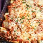 baked cheesy beef stuffed shells in a casserole dish. The pasta is topped with golden brown melted cheese and garnished with chopped basil.