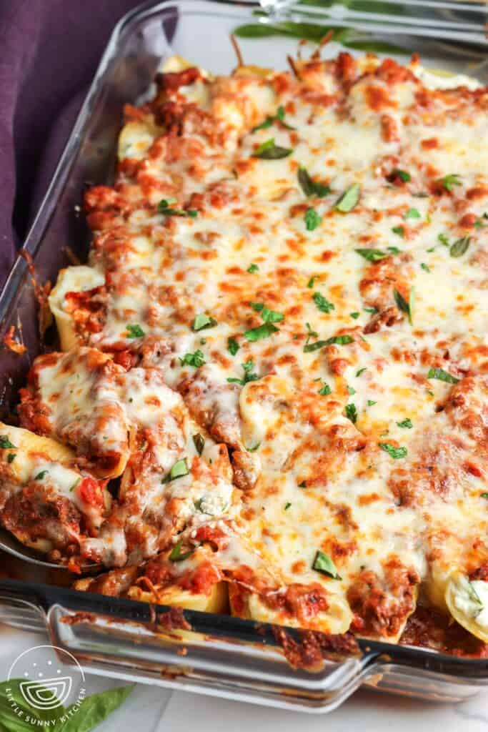 baked cheesy beef stuffed shells in a casserole dish. The pasta is topped with golden brown melted cheese and garnished with chopped basil.