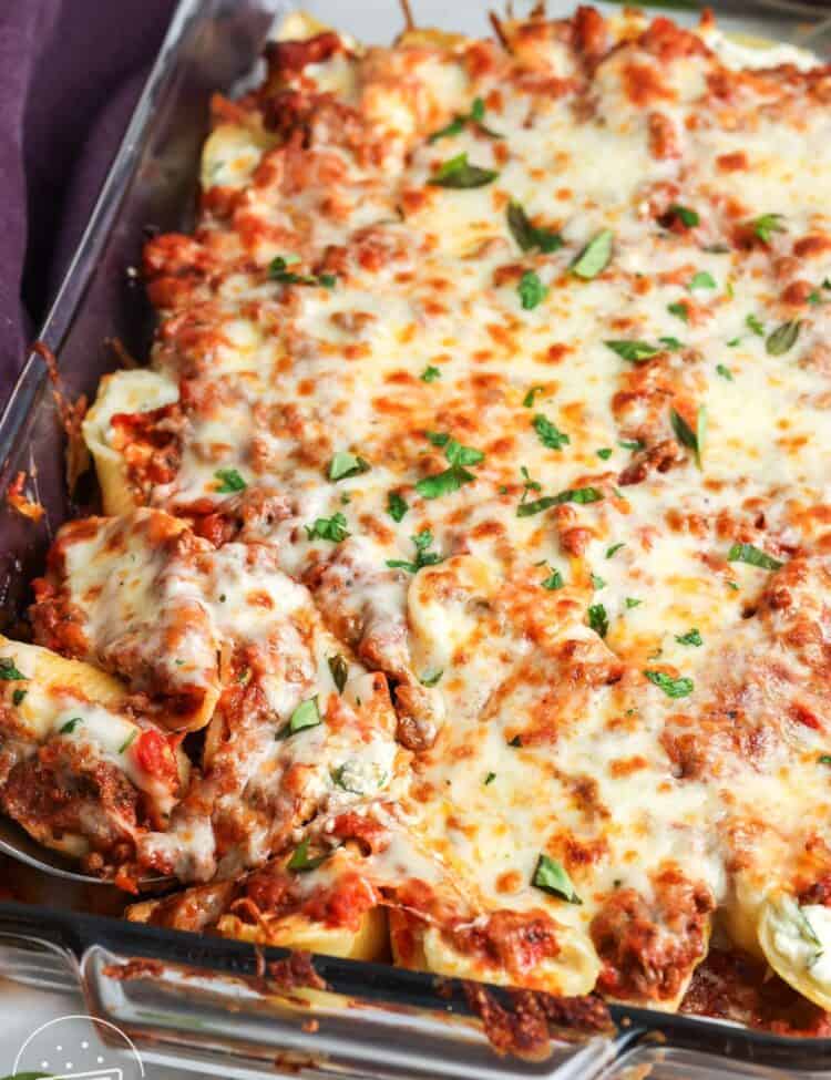 baked cheesy beef stuffed shells in a casserole dish. The pasta is topped with golden brown melted cheese and garnished with chopped basil.
