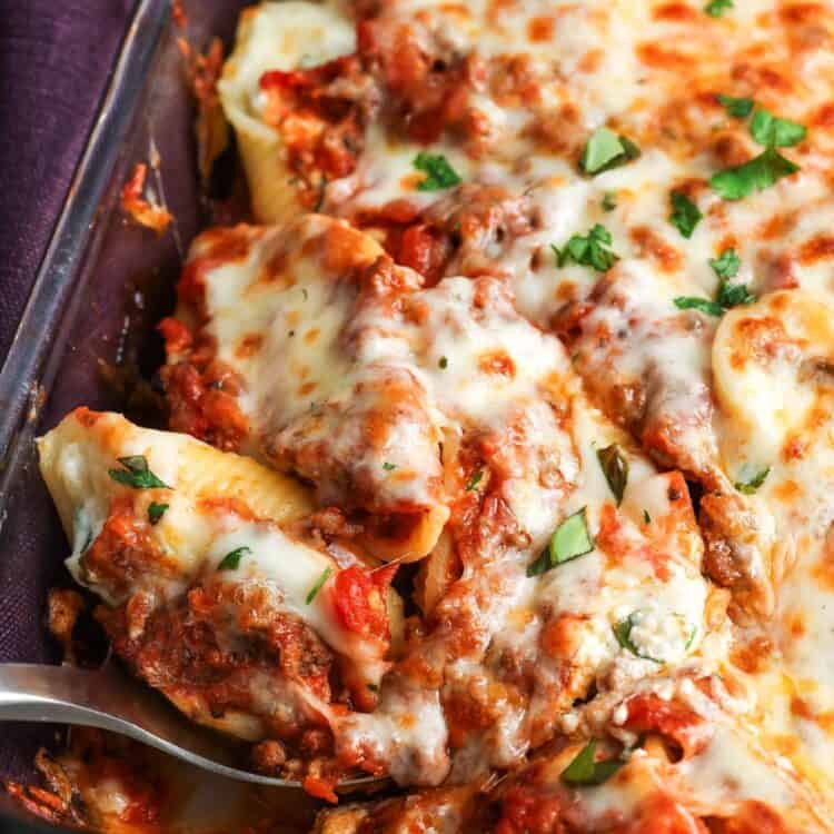 closeup of a pan of stuffed shells with beef and ricotta. A serving is being spooned out of the pan.