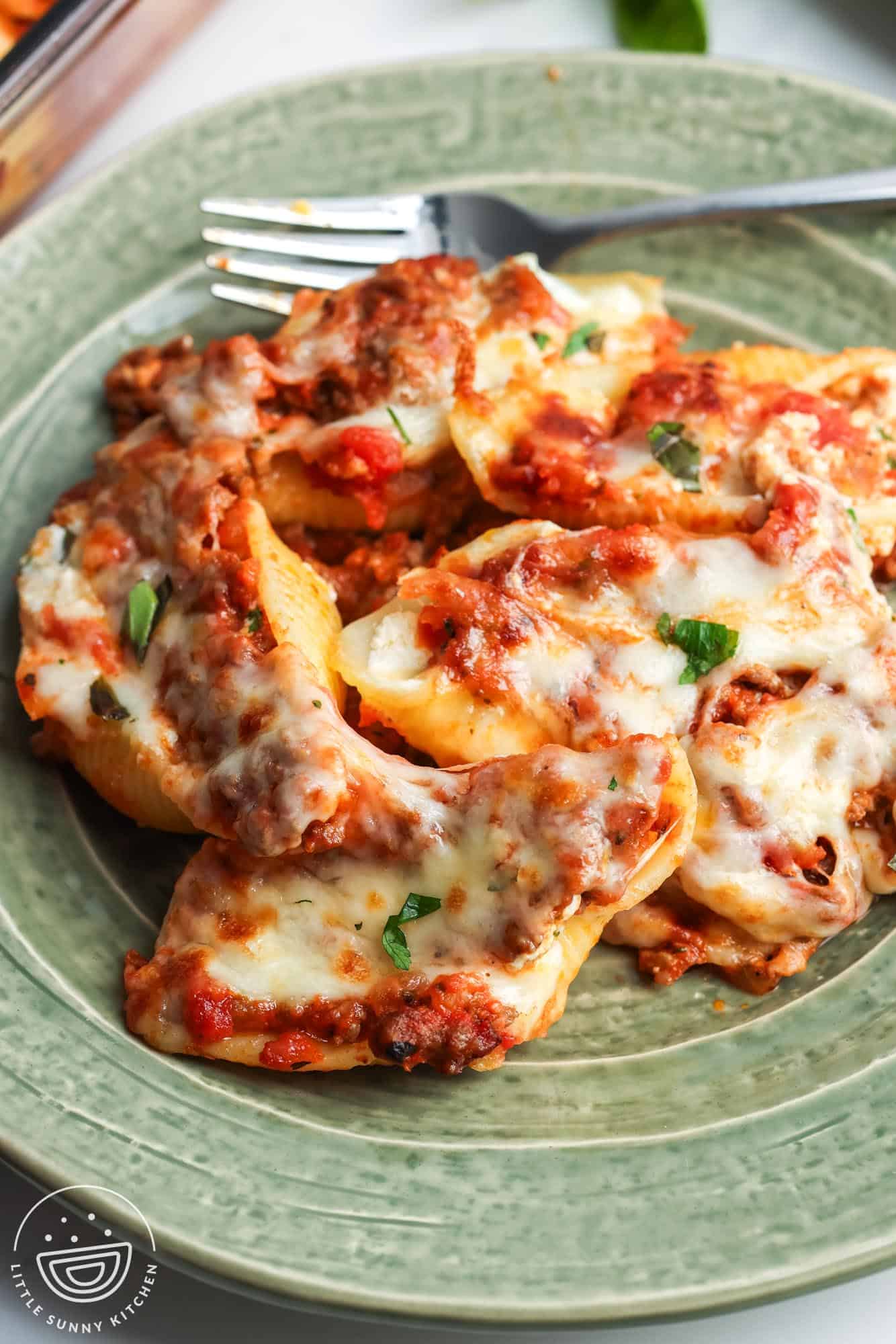 a serving of 5 stuffed shells with meat sauce, topped with mozzarella cheese, on a green dinner plate with a fork.
