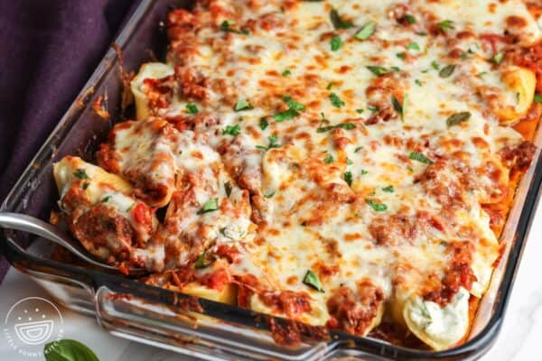 closeup of a pan of stuffed shells with beef and ricotta. A serving is being spooned out of the pan.
