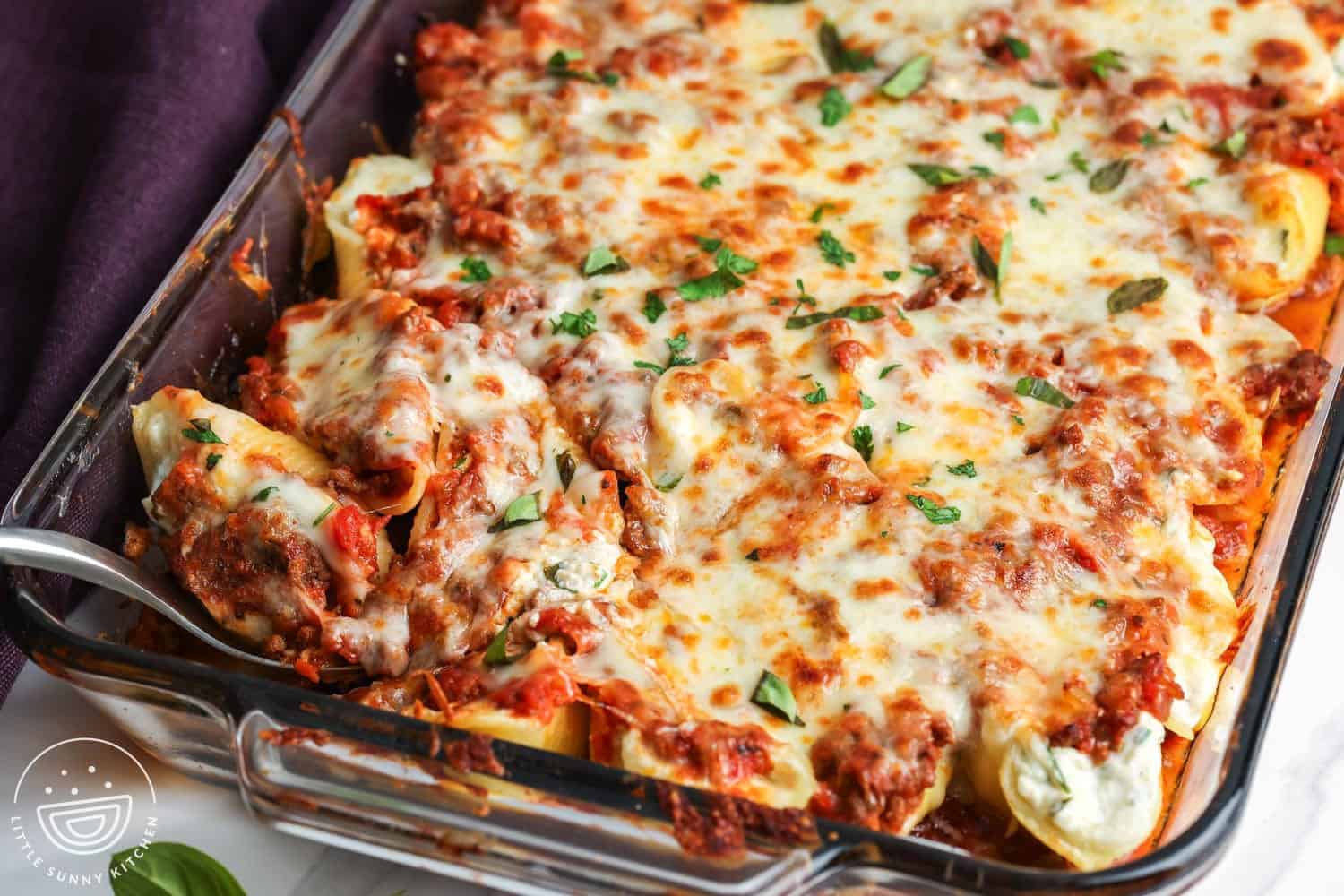 closeup of a pan of stuffed shells with beef and ricotta. A serving is being spooned out of the pan.
