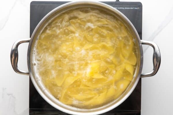 large pasta shells cooking in boiling water in a stainless steel pot.