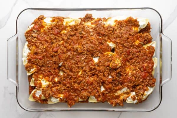 additional meatsauce covering cheese stuffed shells in a glass baking dish.