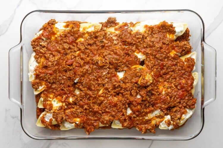 additional meatsauce covering cheese stuffed shells in a glass baking dish.