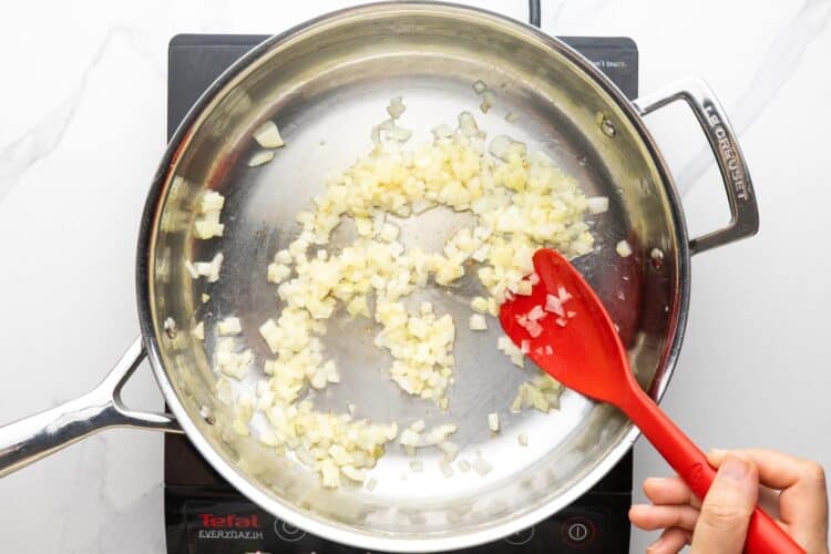 diced onion sauteed in a stainless steel skillet, stirred with a red spoon.