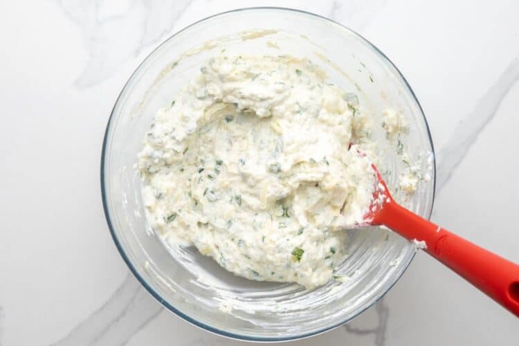 ricotta cheese filling for beef stuffed shells, mixed in a glass bowl with a red spoon.