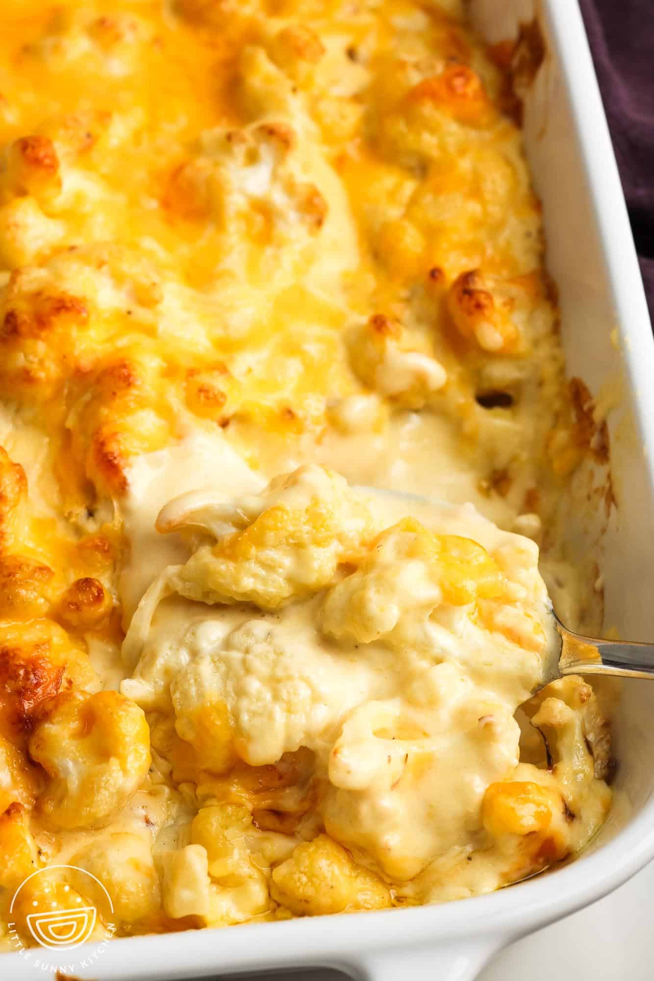 closeup of a baking dish of cauliflower cheese with a thick, creamy sauce.