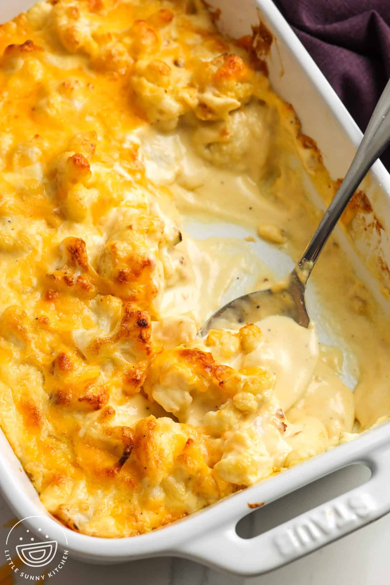 a baking dish of baked cauliflower mac and cheese. Servings have been removed to show the thick, creamy sauce underneath.